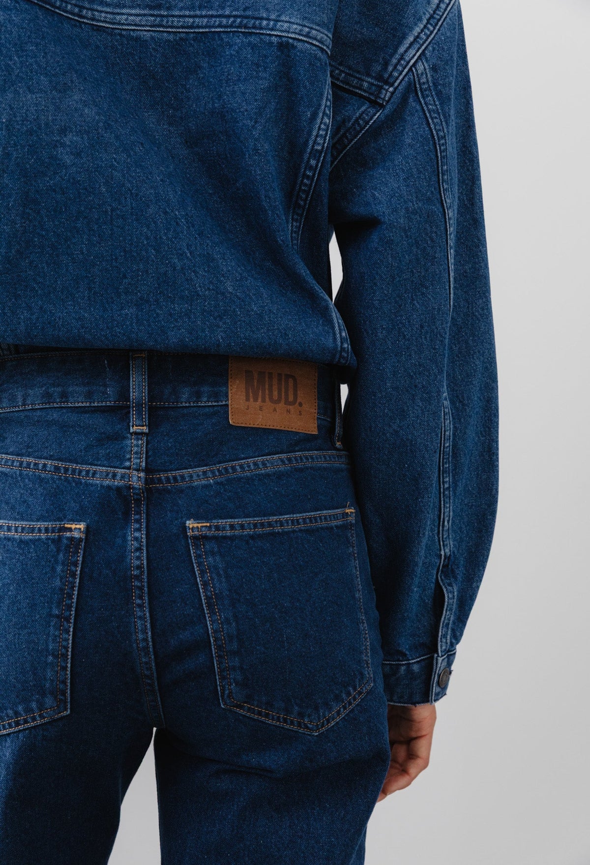 Back view of recycled dark blue denim jacket and jeans set, featuring MUD Jeans logo on leather patch above pocket.