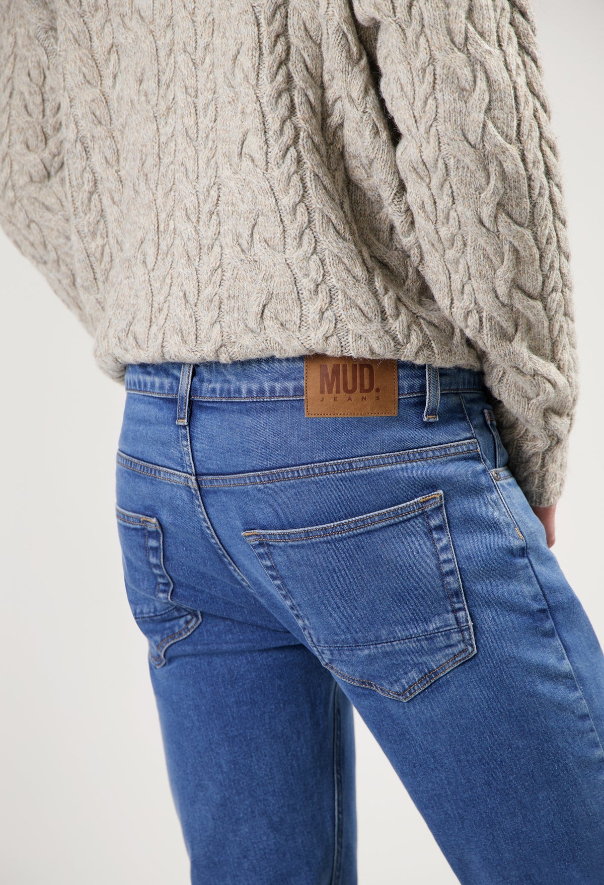 Sustainable MUD Jeans in blue denim, featuring classic fit and eco-friendly design, paired with a beige cable knit sweater.