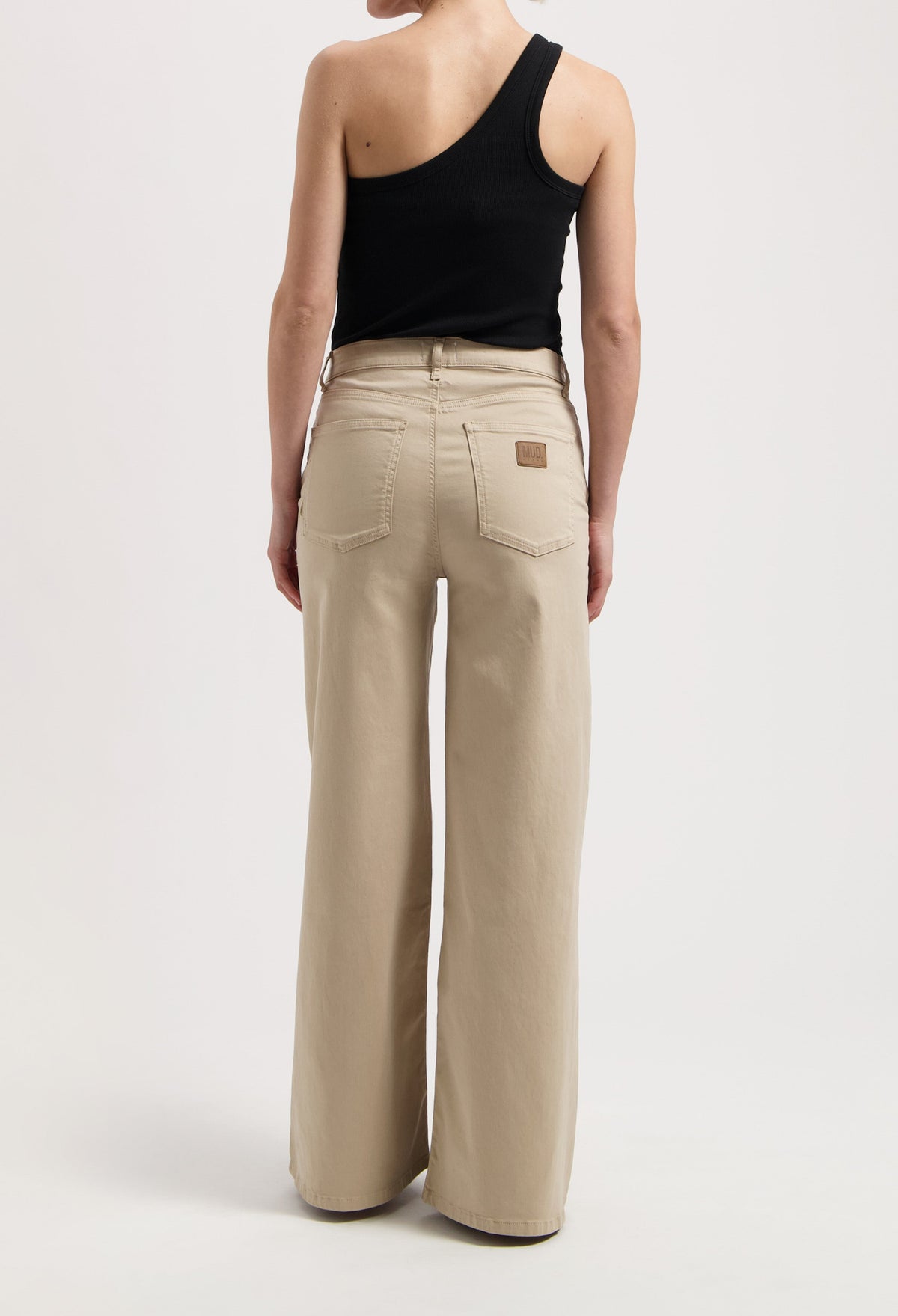 Wide-leg beige MUD Jeans made from organic cotton, worn with a black, one-shoulder sleeveless top in a minimalist style.