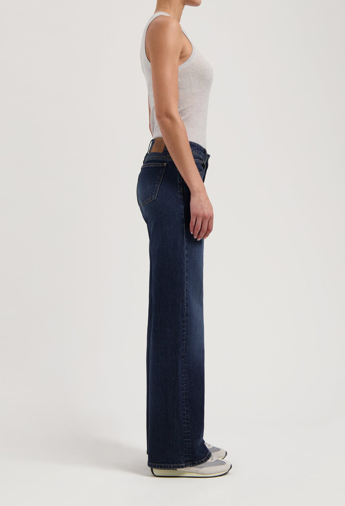Side view of a woman wearing dark blue straight-leg jeans and a light gray tank top, emphasizing casual fashion style.