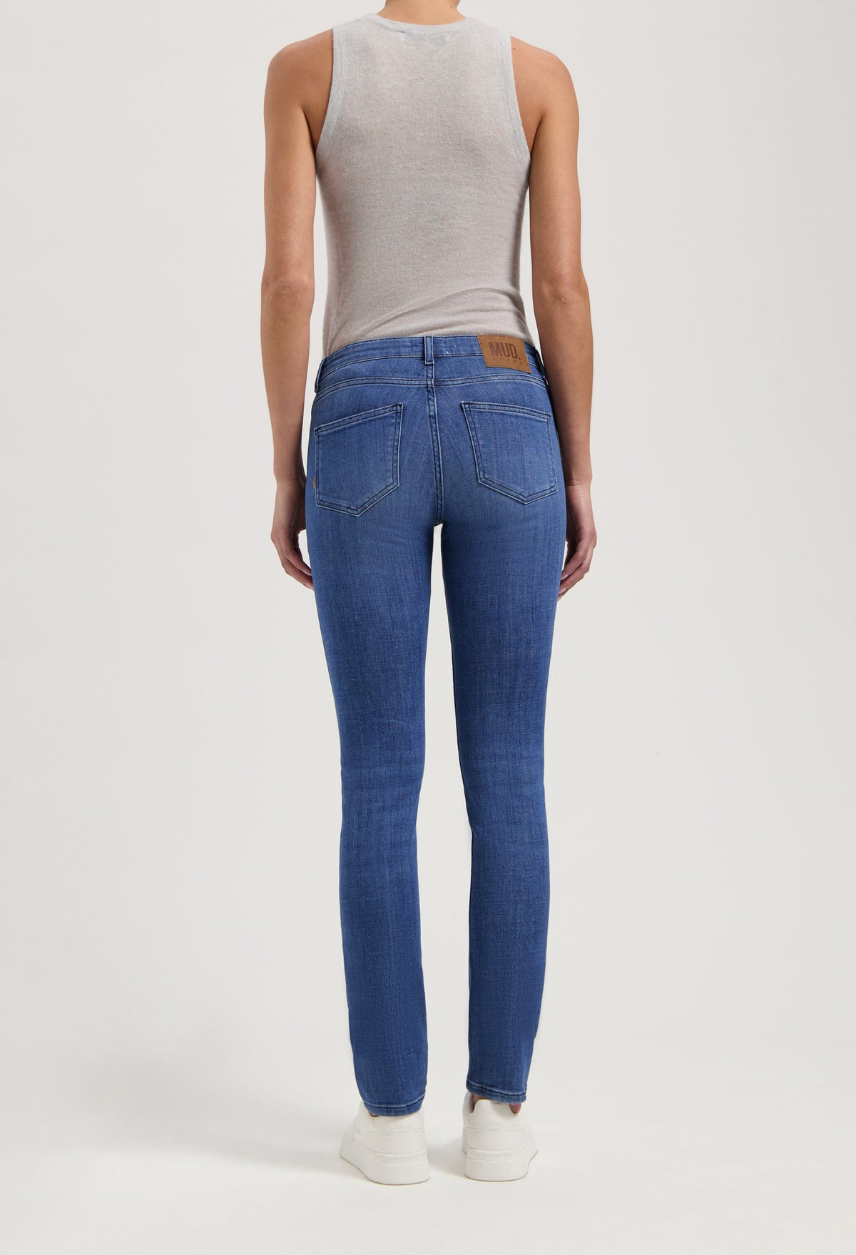 Back view of person wearing straight-fit MUD Jeans in classic blue denim, with a sleeveless gray top and white sneakers.