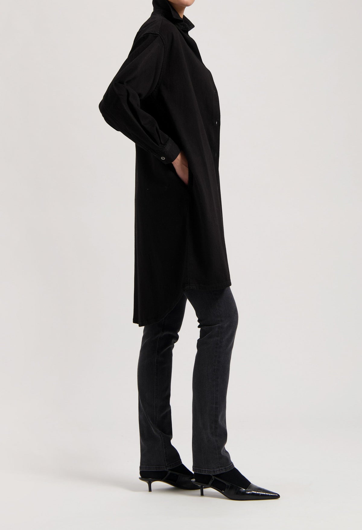 Black oversized shirt dress paired with dark gray, straight-leg jeans and pointed black kitten heels.