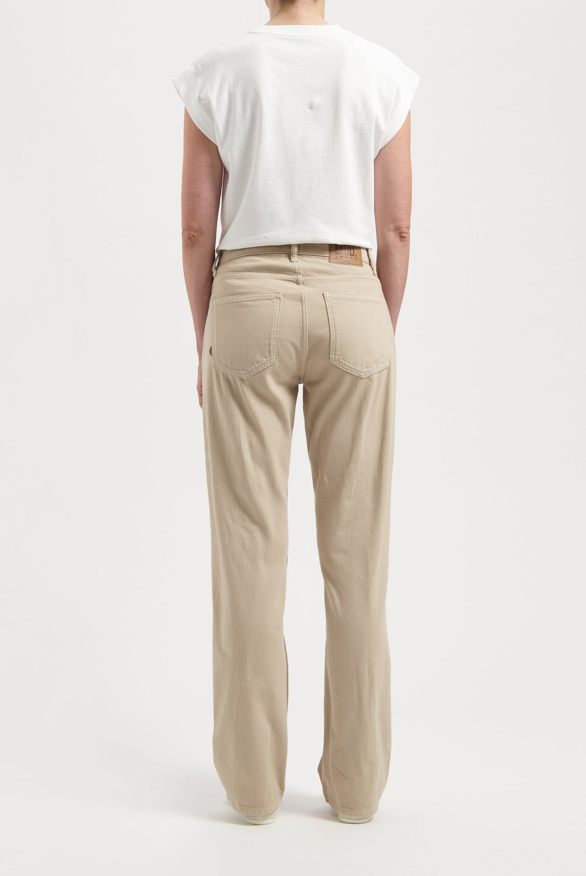 Person wearing beige high-waist denim jeans with relaxed fit, paired with a casual white sleeveless top against a plain background.