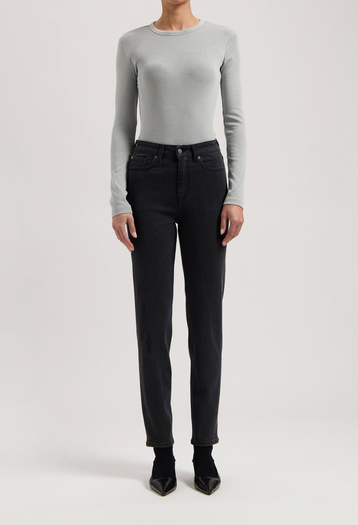 Gray long-sleeve top paired with high-waisted black jeans and pointed black shoes, showcasing a modern minimalist outfit.