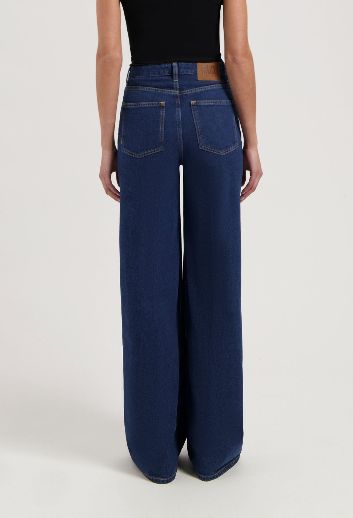 Wide-leg blue denim jeans from MUD Jeans made from organic cotton, shown from the rear, paired with a sleeveless black top.