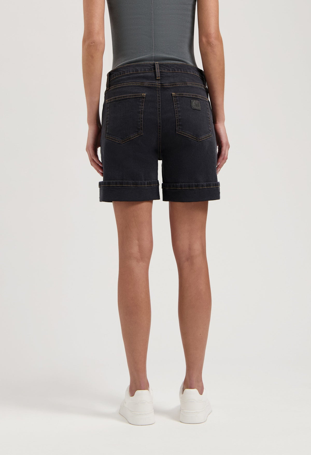 Dark denim shorts with rolled cuffs worn with a fitted gray top, highlighting casual summer fashion in white sneakers.