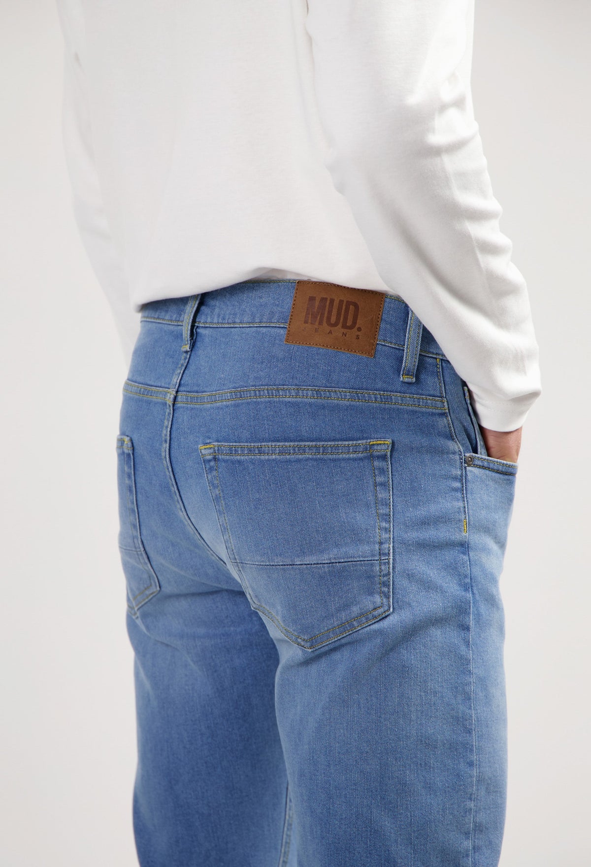 Sustainable MUD Jeans in light blue denim, crafted from organic cotton, paired with a casual gray shirt and white sneakers.