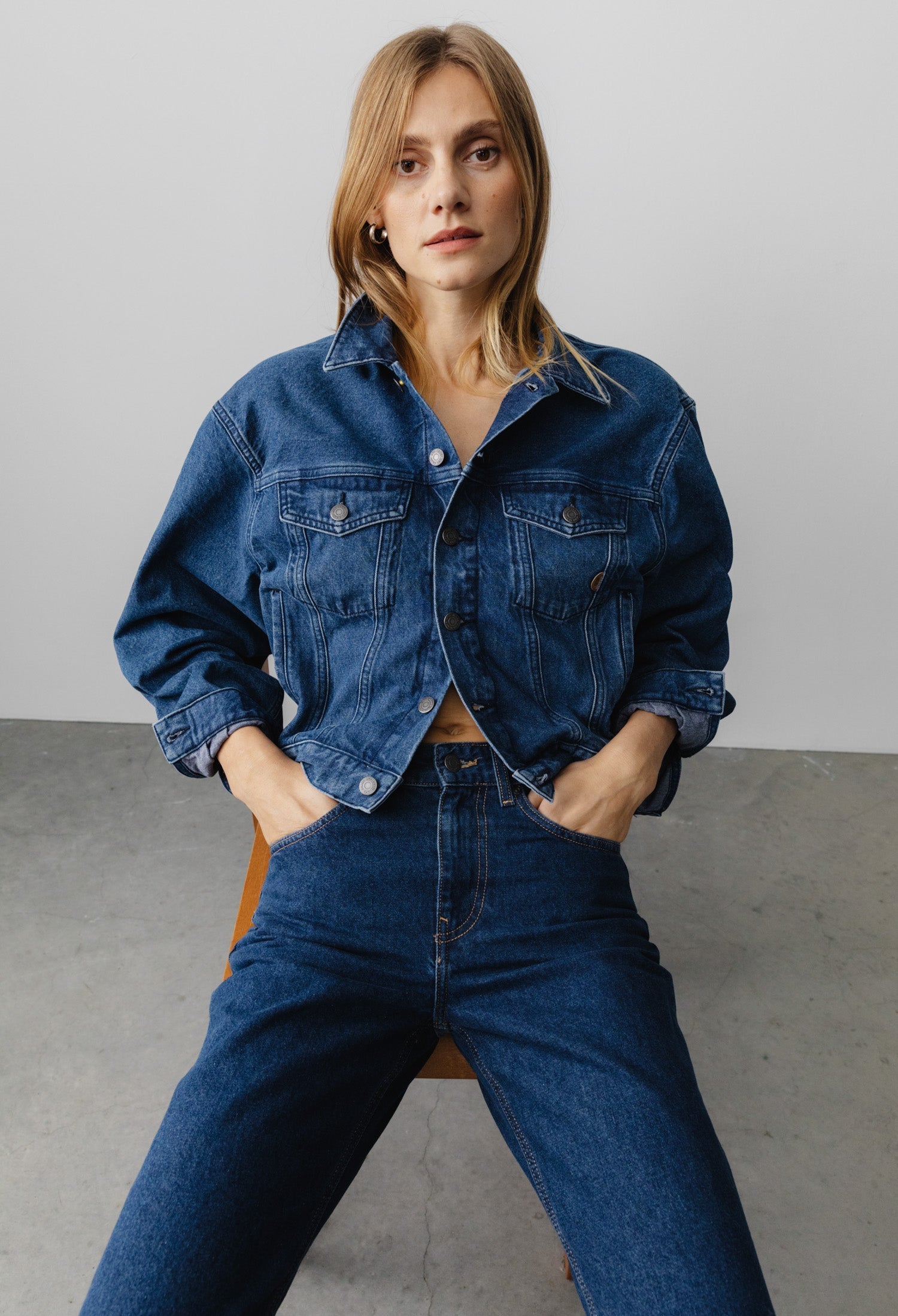 Woman wearing a classic denim jacket with matching high-waisted jeans, styled in a casual fashion on a minimalist background.