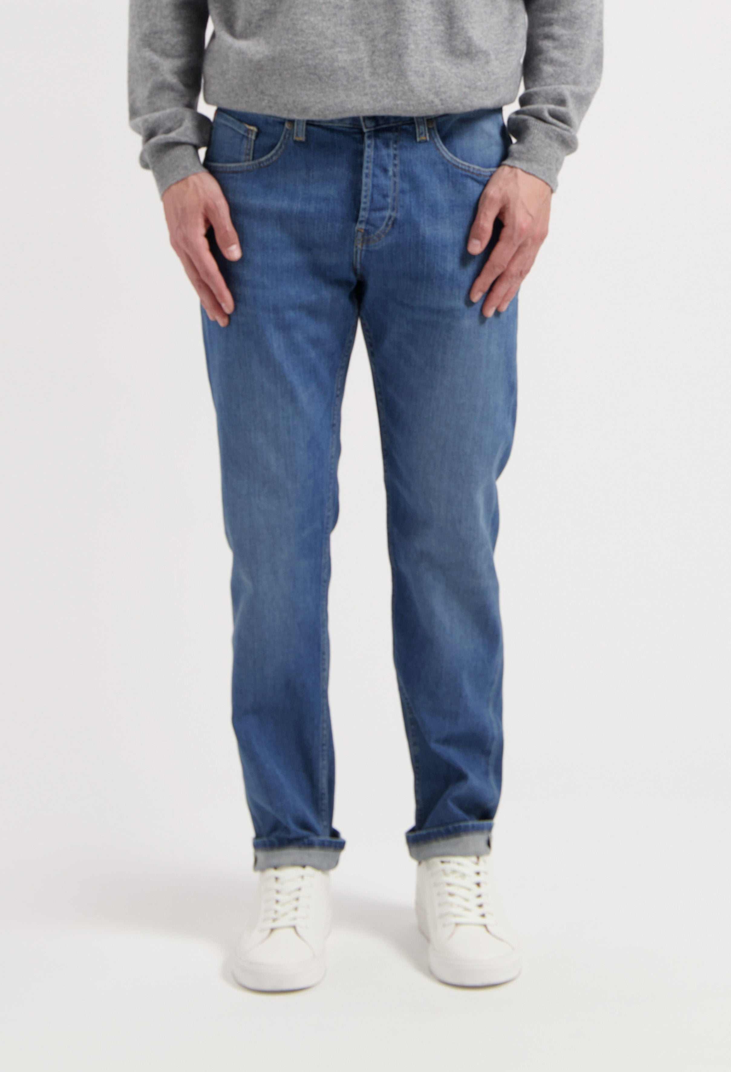 Sustainable MUD Jeans in deep blue denim, paired with an eco-friendly gray sweater and white sneakers, embody ethical fashion.