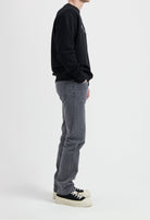 Sustainable MUD Jeans in gray denim, crafted ethically from organic cotton, paired with a black sweatshirt and sneakers.