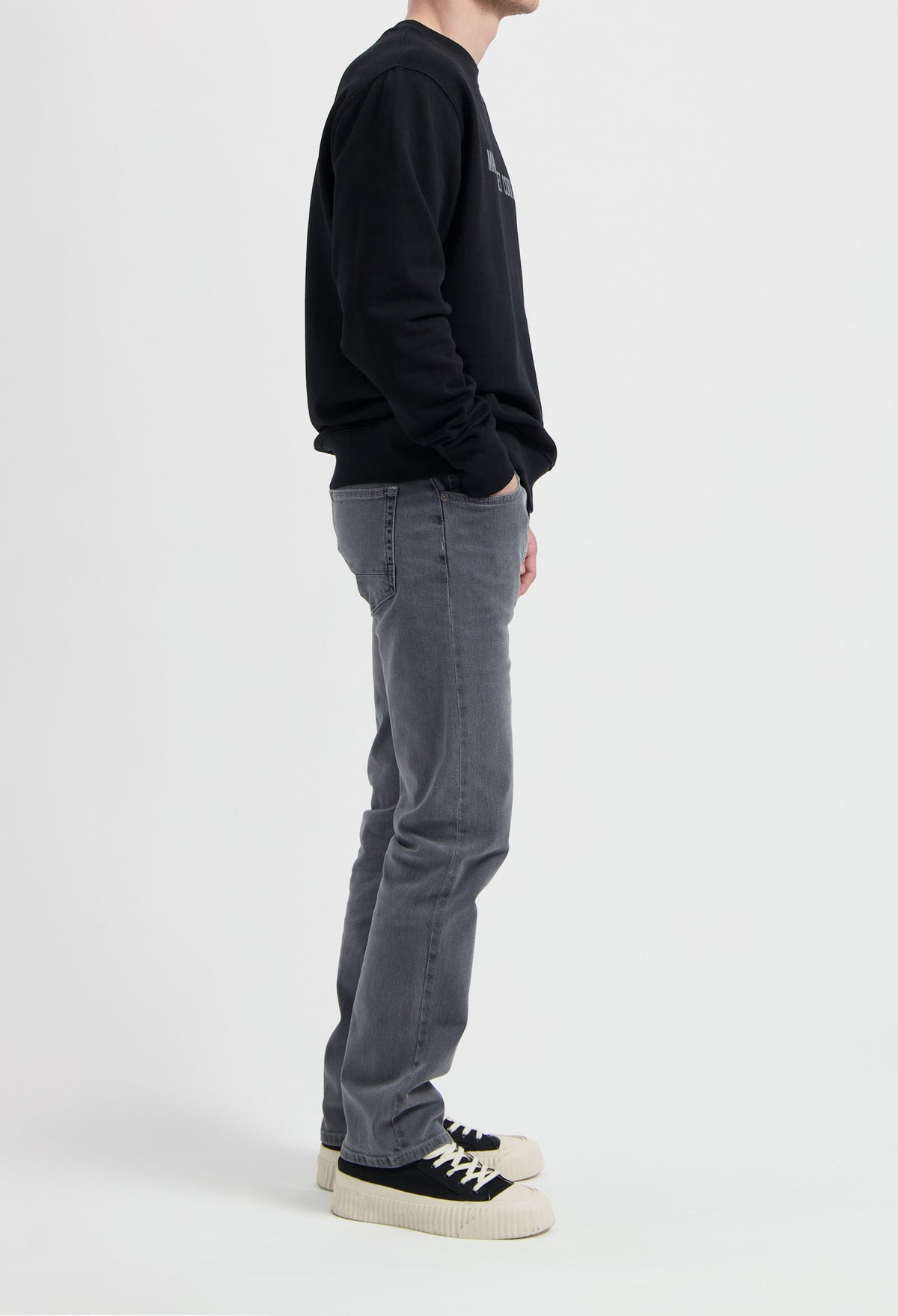 Sustainable MUD Jeans in gray denim, crafted ethically from organic cotton, paired with a black sweatshirt and sneakers.