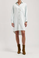 Light blue button-up denim shirt dress with long sleeves, worn with brown suede ankle boots.