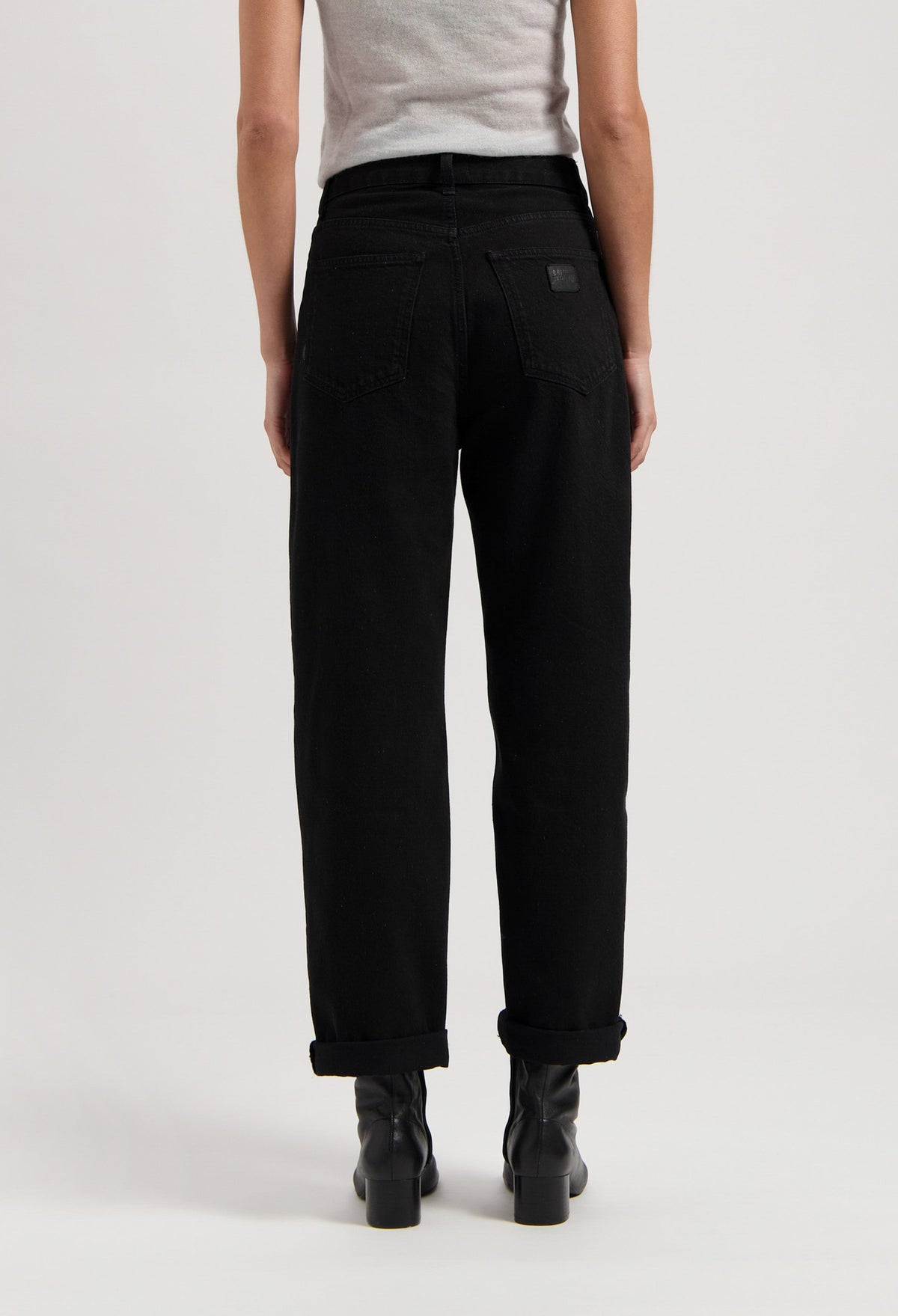Black high-waisted jeans made of cotton, shown from the back, paired with black boots and a light gray sleeveless top.