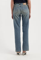 Back view of classic light blue high-waisted jeans paired with white open-back heels on a neutral background.