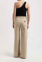 Wide-leg beige MUD Jeans made from organic cotton, worn with a black, one-shoulder sleeveless top in a minimalist style.