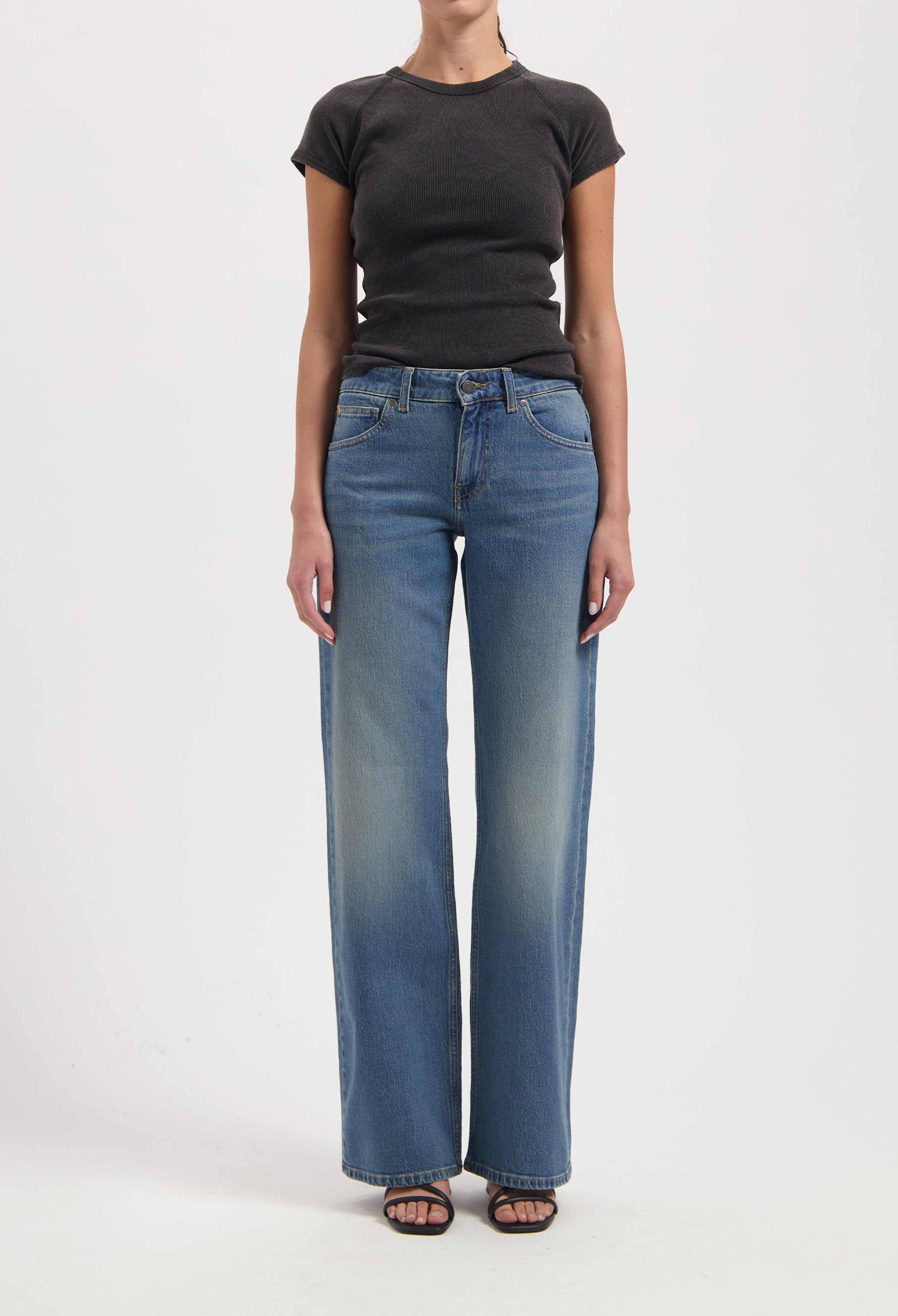 Wide-leg blue jeans with faded effect, paired with a fitted black short-sleeve top, worn by a model against a plain background.