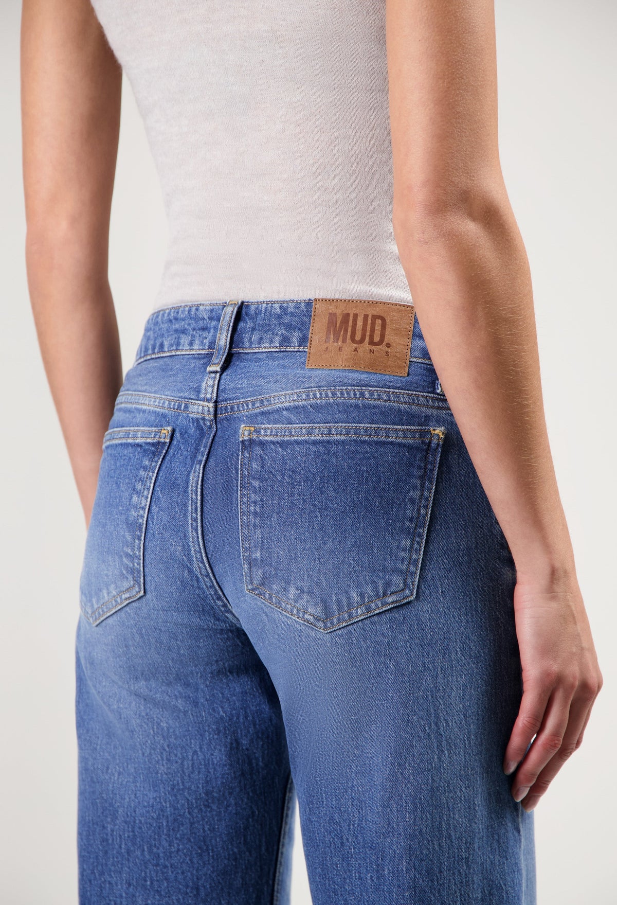 Light blue MUD Jeans from organic cotton, showcasing a close-up of high-rise fit denim worn with a sleeveless white top.