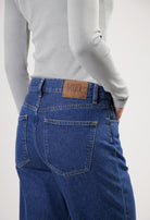 Gray long-sleeve top paired with eco-friendly dark blue MUD Jeans, highlighting back pockets and leather brand patch.