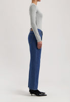 Side view of woman wearing high-waisted blue denim jeans and a light gray long-sleeve top, paired with black heels.