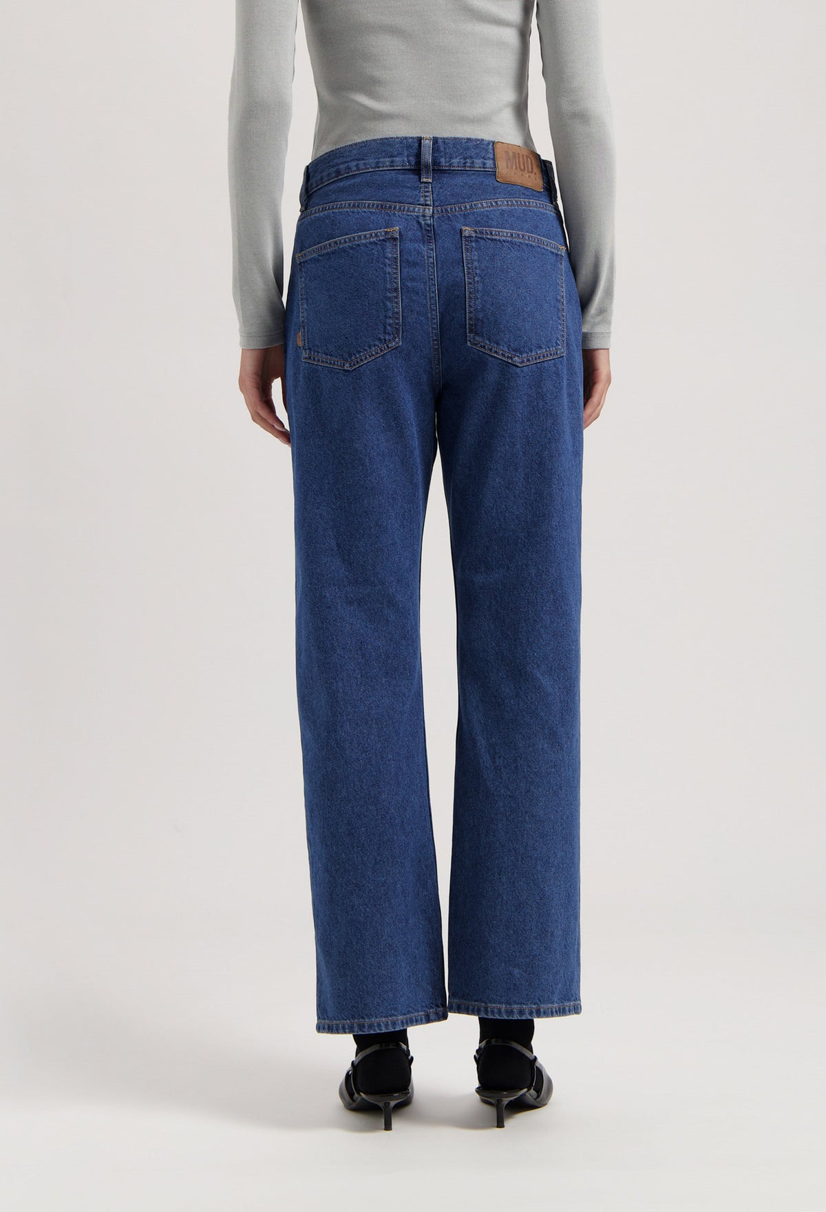 Back view of sustainable MUD Jeans, organic blue denim, wide-leg fit, paired with a light gray long-sleeve top.