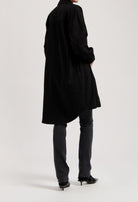 Long black shirt dress styled over dark denim jeans and black pointed-toe heels, showcasing a minimalist fashion look.