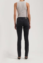 Rear view of black slim-fit denim jeans paired with a sleeveless gray top, showcased in a minimalist style.
