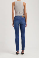 Back view of slim-fit, sustainable blue jeans by MUD Jeans, paired with a light gray sleeveless top and black sandals.