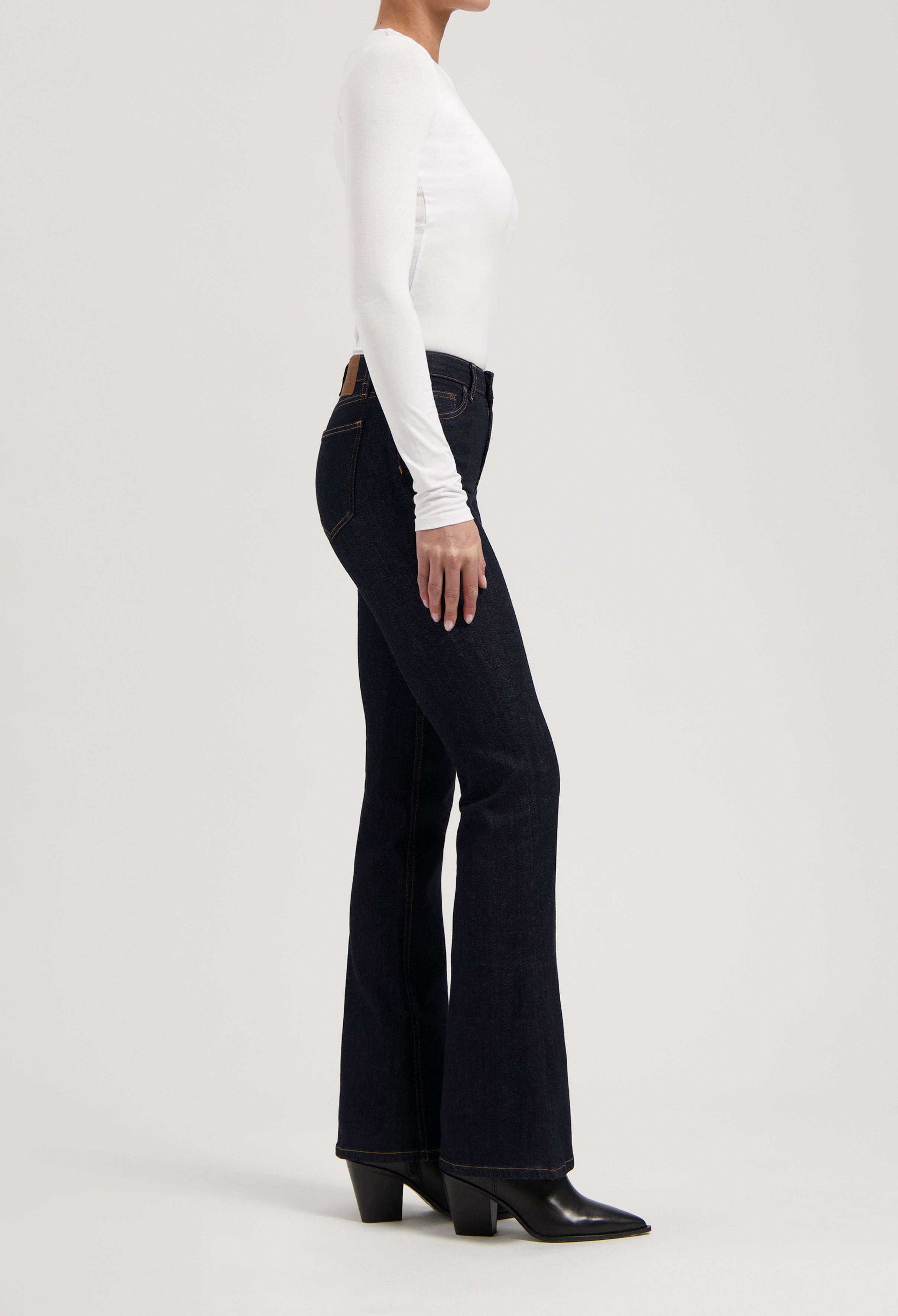 Model wearing dark blue flare jeans paired with a fitted white long-sleeve top and black heeled ankle boots.