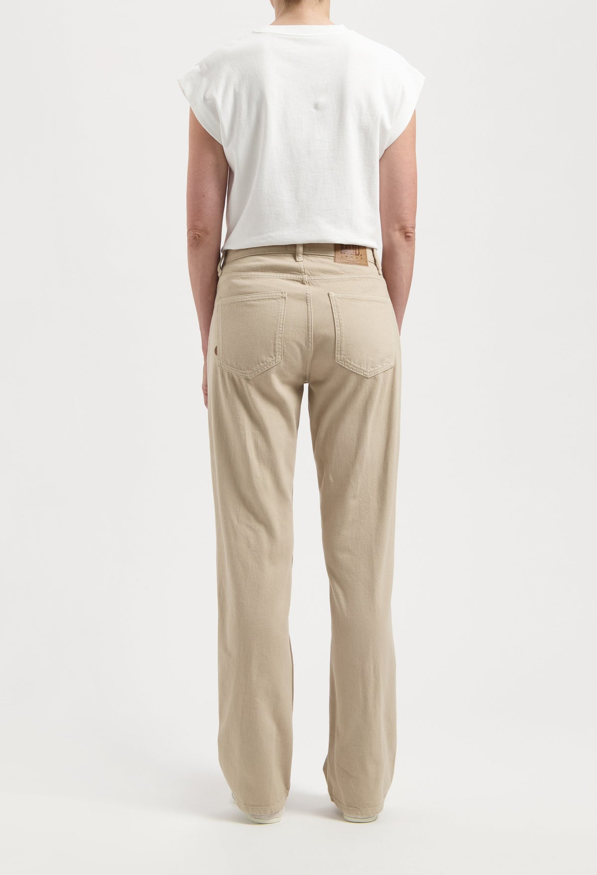 Person wearing beige high-waist denim jeans with relaxed fit, paired with a casual white sleeveless top against a plain background.