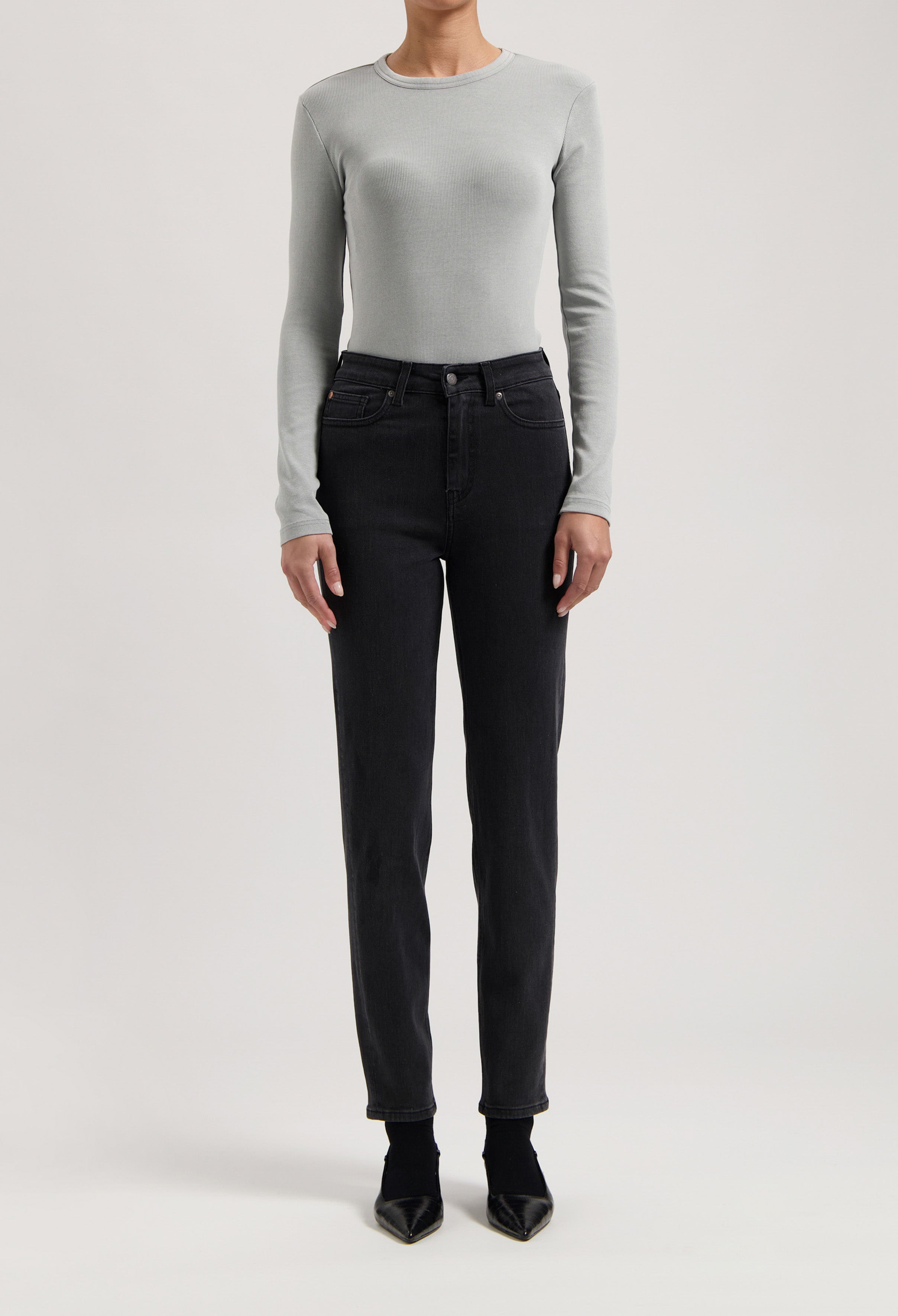 Gray long-sleeve top paired with high-waisted black jeans and pointed black shoes, showcasing a modern minimalist outfit.