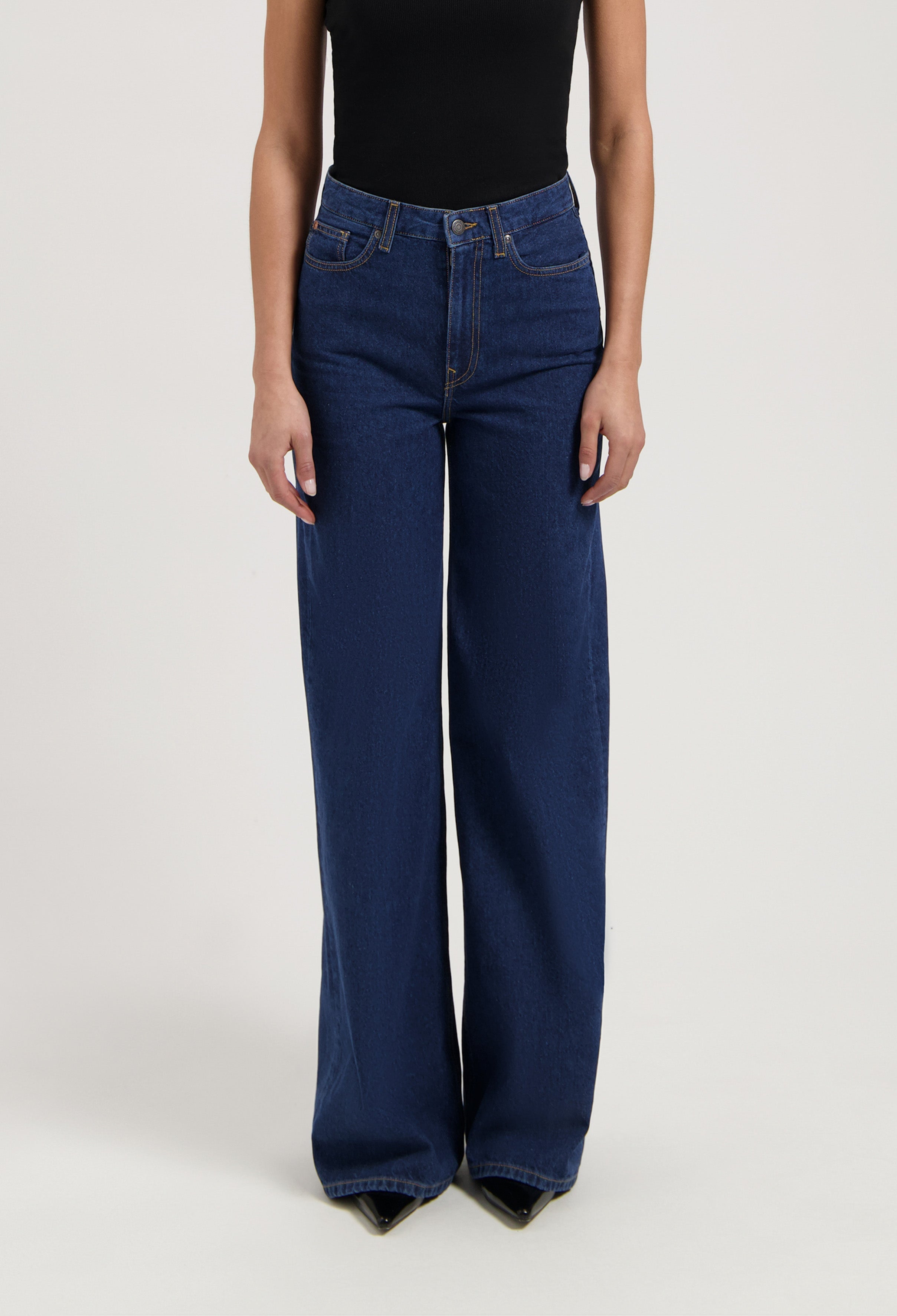 Wide-leg blue denim jeans paired with a black sleeveless top, showing high-waisted style and casual elegance.