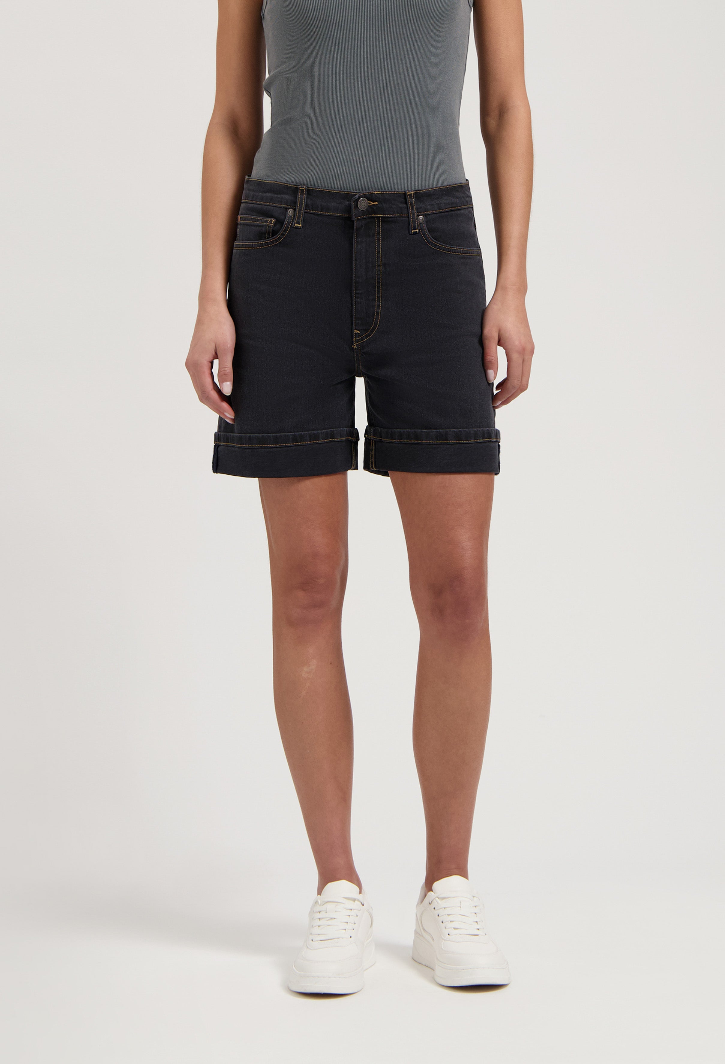 Dark denim shorts with rolled cuffs, paired with a gray ribbed tank top and white sneakers, showing a casual summer look.