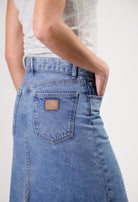Close-up of light blue denim jeans with a leather MUD patch, worn with a fitted white top, showcasing casual style.