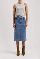 Mid-length denim skirt in blue paired with a sleeveless gray top, styled with brown suede ankle boots on a white background.