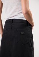 A close-up of a person wearing a fitted black denim skirt paired with a light gray sleeveless top, showcasing minimalist style.